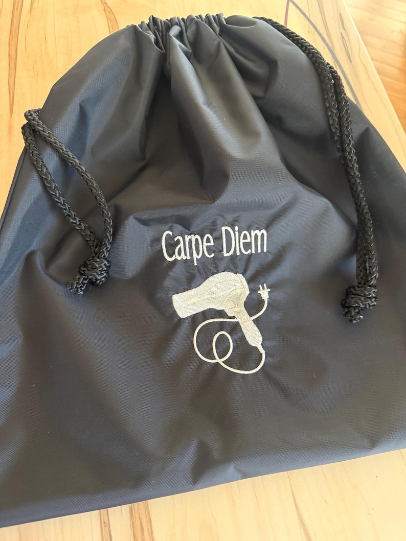 May include: Black drawstring bag with a white embroidered hairdryer and the text "Carpe Diem".