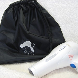 May include: A white hair dryer with the text "Tour Ionic Nano-iSX" on the side. The hair dryer is next to a black drawstring bag with a white embroidered image of a hair dryer and the letters "CY".