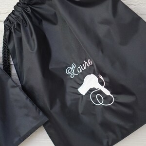 May include: Black drawstring bag with a white embroidered hairdryer and the name "Laure" on it.