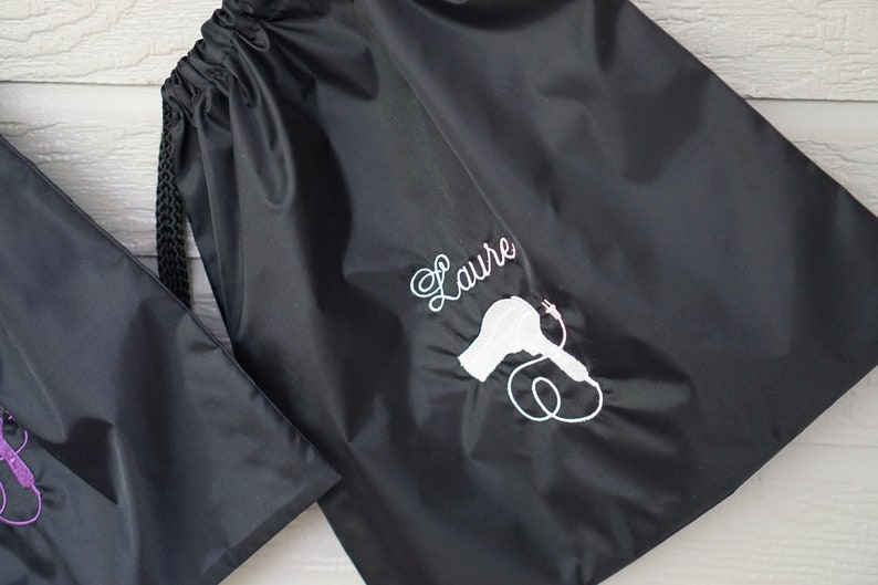 May include: Black drawstring bag with a white embroidered hairdryer and the name "Laure" on it.