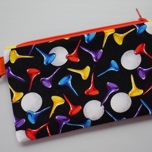May include: A black zippered pouch with a colorful golf ball and tee design. The pouch has a bright orange zipper and a silver key ring.