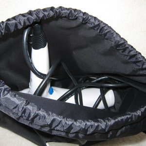 May include: A white handheld steamer with a black cord is stored in a black drawstring bag.