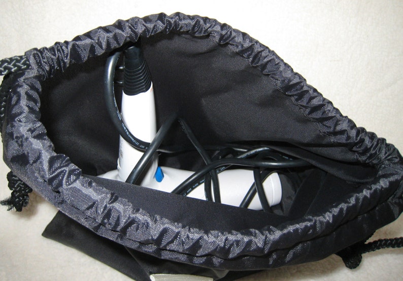 May include: A white handheld steamer with a black cord is stored in a black drawstring bag.