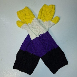 May include: A pair of knitted mittens in the non-binary pride flag colors: yellow, white, purple, and black. The mittens have a cable knit design on the white and purple sections. The yellow section covers the fingers.