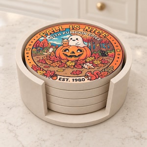 Puede incluir: Una pila de posavasos redondos de cerámica en un soporte claro. El posavasos superior presenta una colorida ilustración otoñal con una calabaza, un fantasma con una bebida, una ardilla y el texto FALL IS NICE WITH PUMPKIN SPICE EST. 1980.