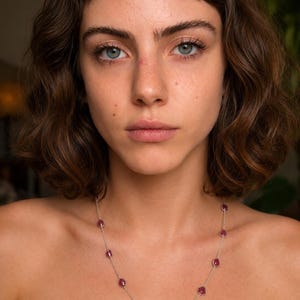 Könnte beinhalten: Eine zarte Silberkettenhalskette mit gleichmäßig verteilten, kleinen, rohen, tief rosa-roten Edelsteinperlen. Die Halskette liegt auf dem Schlüsselbein und zeigt ein minimalistisches Design mit einer dünnen Metallgliederkette und polierten Steinen.