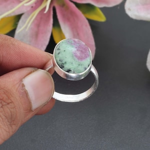 Könnte beinhalten: Ein Silberring mit einem runden, polierten Zoisit-Edelstein, der markante Einschlüsse von rosa Rubin und dunkelgrünen Mineralflecken aufweist und in einer glatten, schlichten Metallfassung sitzt.