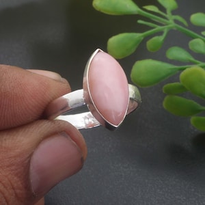 Könnte beinhalten: Ein Silberring mit einem glatten, marquiseförmigen rosa Stein in einer polierten Metallschiene. Die Innenseite der Ringschiene ist deutlich mit der Zahl 925 gestempelt, was auf die Zusammensetzung aus Sterlingsilber hinweist.