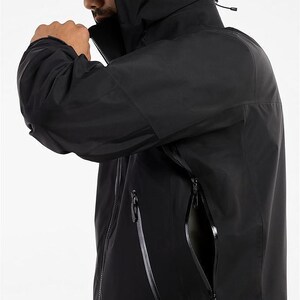May include: Black hooded jacket with a high collar and multiple zippered pockets. The jacket has a sleek, modern design, with a focus on functionality and weather protection. The jacket is made of a durable, water-resistant material.