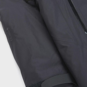 Puede incluir: Primer plano de una manga de chaqueta gris oscuro. La manga presenta una cremallera negra, un pu&ntilde;o de velcro y el logotipo GORE-TEX. La chaqueta parece estar hecha de un material duradero e impermeable, adecuado para actividades al aire libre.