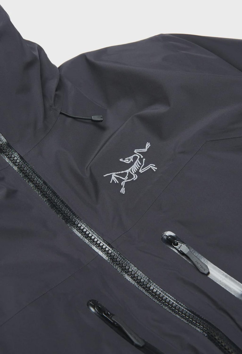 Puede incluir: Chaqueta con capucha gris oscuro con cremallera completa y un peque&ntilde;o logotipo blanco en el pecho. La chaqueta tiene un dise&ntilde;o elegante con cuello alto y capucha con cord&oacute;n. La cremallera es negra y tiene un dise&ntilde;o texturizado.