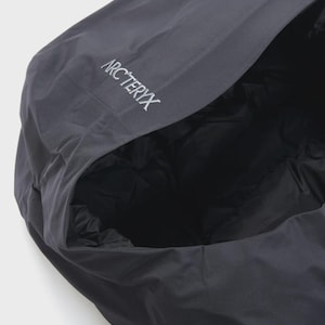 Puede incluir: Primer plano de una chaqueta con capucha gris oscuro con el nombre de la marca "Arc'teryx" bordado en blanco en la capucha. El interior de la capucha es negro y acolchado. La chaqueta parece estar hecha de un material duradero y resistente a la intemperie.