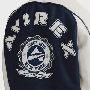 May include: A navy blue and white varsity jacket with the text "AIR FORCE NEW YORK CLASSIC SINCE 1975" on the back. The jacket has white accents and patches.