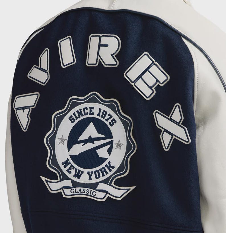 May include: A navy blue and white varsity jacket with the text "AIR FORCE NEW YORK CLASSIC SINCE 1975" on the back. The jacket has white accents and patches.