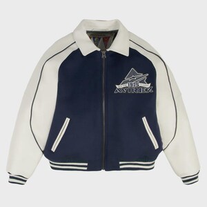 May include: A navy blue and white varsity jacket with a zip-up front. The jacket features white sleeves, a white collar, and a striped hem and cuffs. The chest displays the text "AVIREX 1975 CLASSIC" with a mountain graphic.
