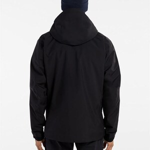 May include: A black hooded jacket with a navy blue beanie. The jacket has a full-length zipper and long sleeves. The person is facing away from the camera, and the background is plain white.