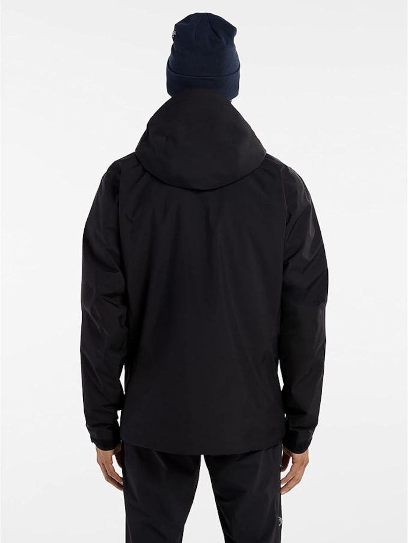 May include: A black hooded jacket with a navy blue beanie. The jacket has a full-length zipper and long sleeves. The person is facing away from the camera, and the background is plain white.