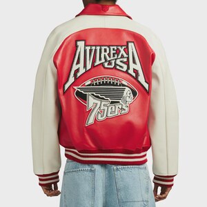 May include: A red and cream-colored letterman jacket with the text "AVIREX USA" and a football graphic on the back. The jacket has a ribbed hem and cuffs with red and white stripes. The jacket also has the text "75ers".