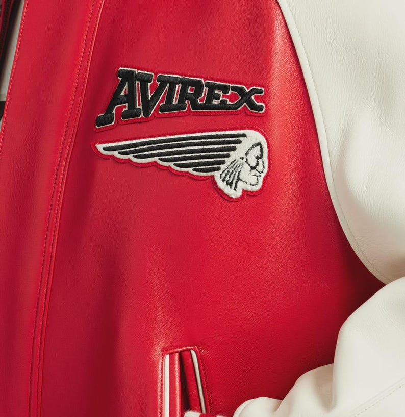 May include: Red leather jacket with white sleeves. The jacket features the embroidered text "AVIREX" above a patch with a Native American head and wing design. The jacket has a classic varsity style.