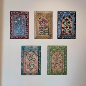Puede incluir: Cinco obras de arte murales rectangulares con diseños florales. Cada pieza presenta un marco de diferente color, incluyendo burdeos, dorado, azul, turquesa y verde. La obra de arte dentro de cada marco representa un arreglo floral con flores rosas o rojas.