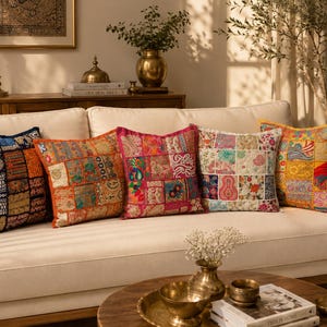 May include: Five decorative throw pillows on a cream-colored sofa. The pillows feature a patchwork design with various colors and patterns, including blue, orange, pink, white, and yellow. The pillows add a touch of color and texture to the living room setting.