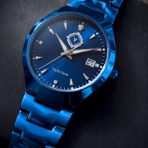 May include: A blue wristwatch with a matching band. The watch face is dark blue with silver-tone hands and markers, and a date display at the 3 o'clock position. The watch has the word "Valirium" on the face.
