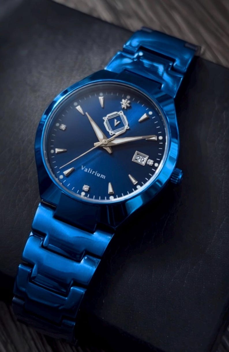 May include: A blue wristwatch with a matching band. The watch face is dark blue with silver-tone hands and markers, and a date display at the 3 o'clock position. The watch has the word "Valirium" on the face.