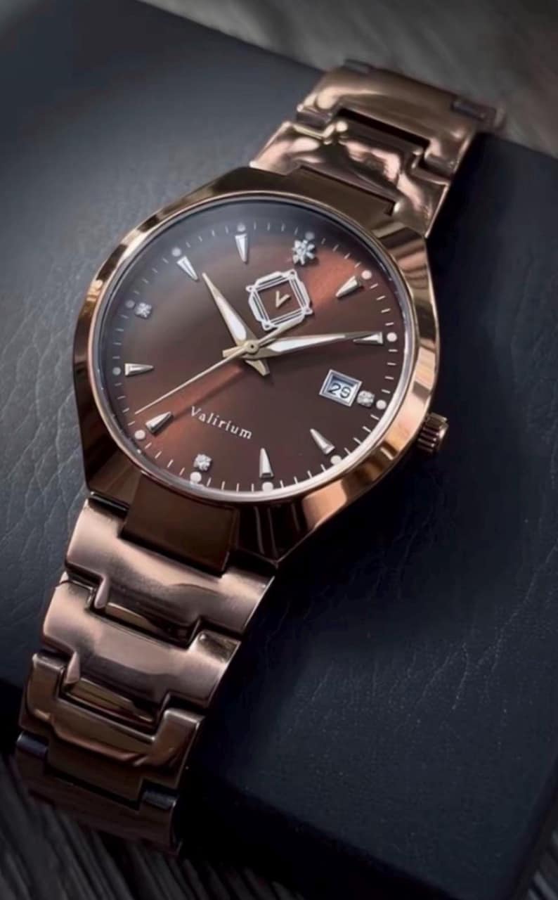 May include: A rose gold wristwatch with a brown face and matching band. The watch face features silver-colored hands and markers, a date display, and the brand name "Valirium". The watch is set against a dark background.