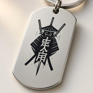 Könnte beinhalten: Ein silberfarbener Hundeanhänger-Schlüsselanhänger aus Metall mit einer schwarzen Gravur einer stilisierten Figur mit konischem Hut, zwei gekreuzten Schwertern im Hintergrund und japanischen Kanji-Schriftzeichen in der Mitte.