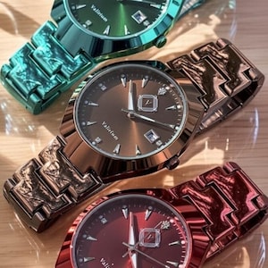May include: Three metallic watches in green, bronze, and red, each with a matching band. The watch faces display the brand name "Valirium" and a date window. The watches are on a light-colored wooden surface.