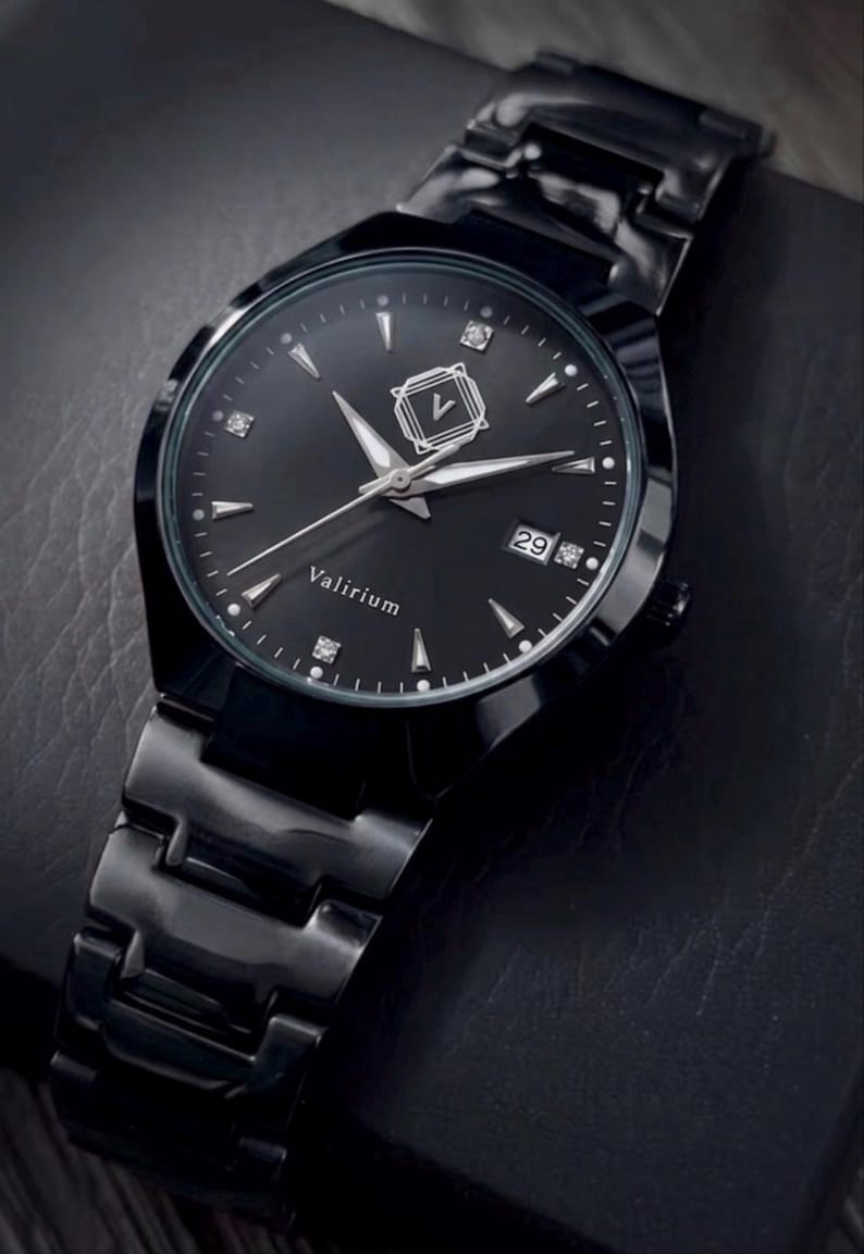 May include: A black wristwatch with a matching black band. The watch face is black with silver hands and markers, and the date is displayed at the 3 o'clock position. The brand name "Valirium" is printed on the watch face.