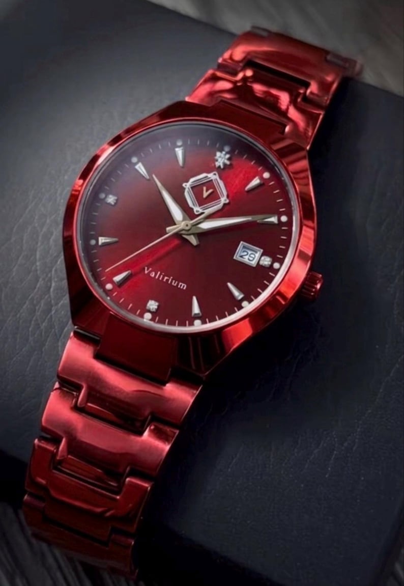 May include: A red wristwatch with a matching band. The watch face is also red, featuring silver-colored hands and markers, and a date display at the 3 o'clock position. The watch has the word "Valirium" printed on the face.