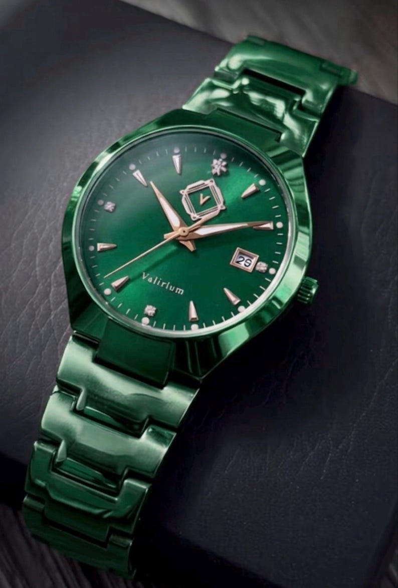 May include: A green wristwatch with a matching band. The watch face is green with gold-colored hands and markers. The date is displayed at the 3 o'clock position. The watch has the word "Valirium" on the face.