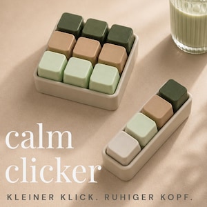 Könnte beinhalten: Ein quadratisches Tablett mit neun würfelförmigen Tasten und ein rechteckiges Tablett mit vier würfelförmigen Tasten in Olivgrün, Beige und Salbeigrün. Der Text calm clicker und KLEINER KLICK. RUHIGER KOPF. ist zu sehen.