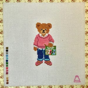 May include: A needlepoint canvas featuring a brown teddy bear wearing a pink sweater and blue jeans. The bear holds a green bag labeled WIP with small colorful icons. A vertical color palette guide is on the left, and a small pink icon is in the corner.