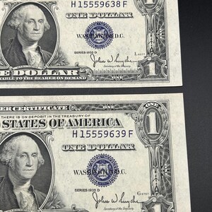 May include: Two United States one dollar silver certificates, series 1935 D, featuring a portrait of George Washington. The bills display the text United States of America, One Dollar, and the signatures of the Secretary of the Treasury.