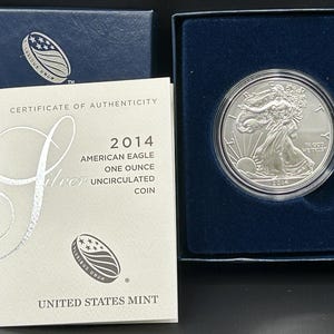 May include: A silver 2014 American Eagle one-ounce uncirculated coin in a protective case. The coin features Lady Liberty and the sun on one side. The certificate of authenticity is visible, along with the United States Mint logo.