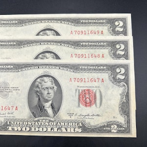 May include: Three United States two-dollar bills from the 1953 series, each featuring a portrait of Thomas Jefferson and a red treasury seal. The serial numbers A 70911647 A, A 70911648 A, and A 70911649 A are printed in red ink on the paper currency.