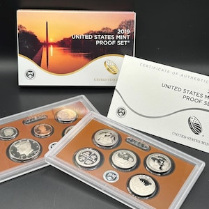 May include: A 2019 United States Mint Proof Set featuring a box with a sunset image of the Washington Monument, a certificate of authenticity, and two clear plastic cases containing various silver-toned and copper-toned proof coins.
