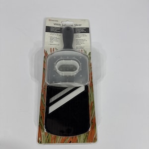 May include: A wide julienne slicer with a black handle and a clear plastic guard. The slicer has a black cutting surface and is packaged on a cardboard backing with text. The packaging features images of carrots.