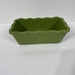 May include: An olive green ceramic baking dish, rectangular with a scalloped edge. The dish has a glossy finish and is empty. The sides slope inwards, and the corners are angled. The dish is on a white surface.