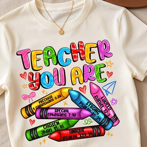 May include: A cream-colored t-shirt featuring the colorful text TEACHER YOU ARE above five crayons in yellow, blue, pink, green, and red. Each crayon displays a word and a Bible verse, including Precious 1 Corinthians 6:20, Strong Psalm 18:35, Lovely Daniel 12:3, Special Ephesians 7:10, Chosen John 15:16, and Unique Psalm 139:14.