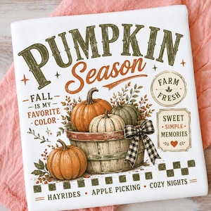 Op de afbeelding: Een wit t-shirt met een afbeelding met de tekst PUMPKIN SEASON, FALL IS MY FAVORITE COLOR, FARM FRESH, SWEET SIMPLE MEMORIES, HAYRIDES, APPLE PICKING, COZY NIGHTS. Het ontwerp toont oranje en groene pompoenen in een mand met een strik.