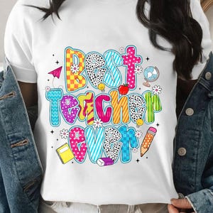 May include: A white t-shirt featuring a colorful graphic with the text "BEST TEACHER EVER" in bold, patterned letters. The design includes illustrations of a paper airplane, a globe, an apple, a notebook, a pencil, an eraser, and small flowers.