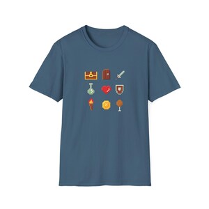 Puede incluir: Camiseta azul con gráficos pixelados de elementos de juegos de fantasía, incluyendo un cofre del tesoro, una puerta, una espada, una botella de poción, un corazón, un escudo, una antorcha, una moneda y una copa. El diseño está centrado.