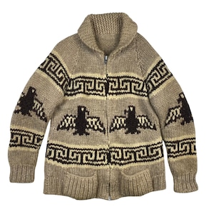 May include: A tan, zip-up cardigan sweater with a shawl collar. The sweater features a geometric pattern in dark brown and cream, along with stylized bird motifs. It has two front pockets and ribbed cuffs and hem.