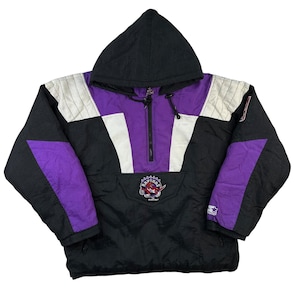 May include: Black, purple, and white hooded anorak jacket. The jacket features a purple center panel with a zipper, white accents, and the Raptors logo. The jacket has a black hood and sleeves, and a Starter logo on the sleeve.