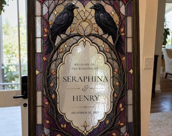 May include: A rectangular wedding sign in a dark wood frame featuring a stained glass design with two black ravens perched on branches. The centre panel displays the text: WELCOME TO THE WEDDING OF SERAPHINA & HENRY OCTOBER 31, 2027.