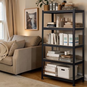 May include: A black metal shelving unit with books, boxes, and ornaments. The shelves are made of light-coloured wood. A beige sofa and framed landscape art are in the background, creating a cosy living space.
