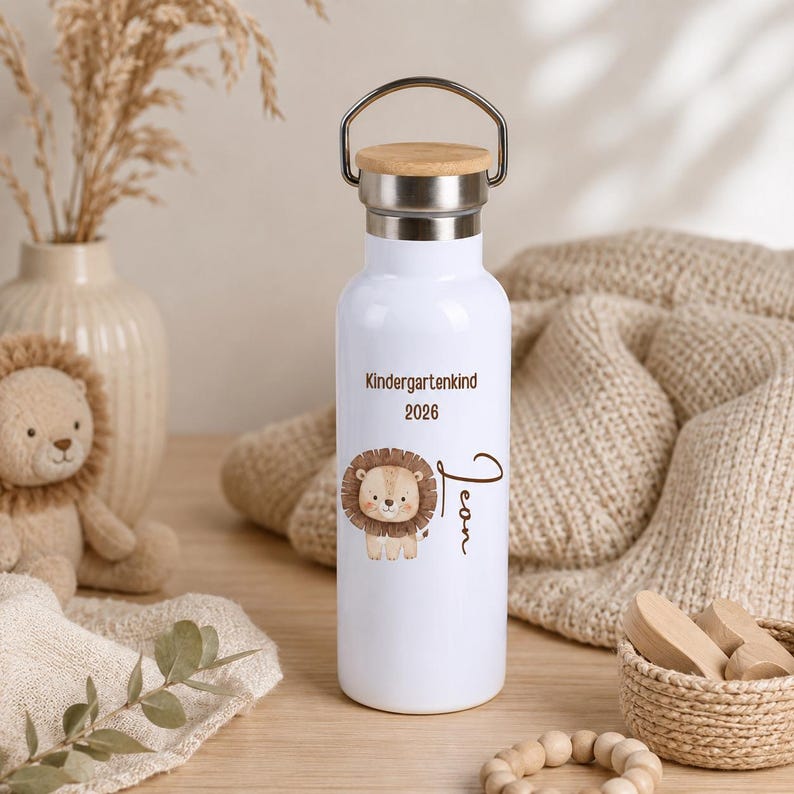 May include: A white metal water bottle with a bamboo lid and a silver handle. The bottle features a brown lion illustration, the text "Kindergartenkind 2026", and the name "Leon" written in a brown cursive script on the front surface.